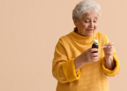 Ill senior woman taking cough syrup on beige background