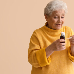 Ill senior woman taking cough syrup on beige background