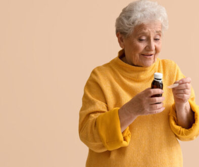 Ill senior woman taking cough syrup on beige background