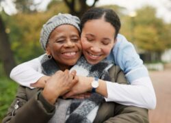 Caregiver, hug and park with old woman in a wheelchair for retirement, elderly care and physical therapy. Trust, medical and healthcare with portrait of patient and nurse in nature for rehabilitation